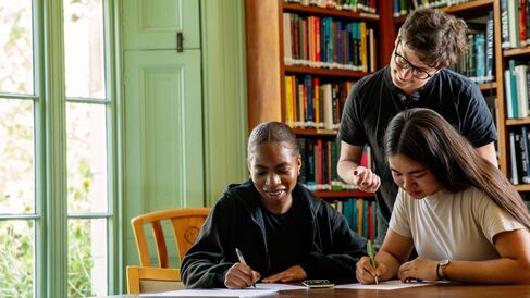 Three University of Cambridge students studying in front of bookshelves. Copyright University of Cambridge