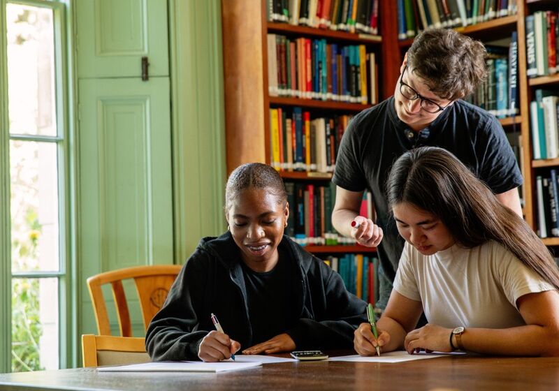 Three University of Cambridge students studying in front of bookshelves. Copyright University of Cambridge (June 2023)
